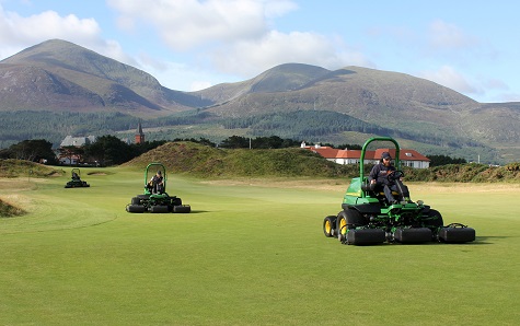 Three of the new John Deere 7500A E-Cut hybrid electric fairway mowers working at The Royal County Down Golf Club, with the Mountains of Mourne in the background.